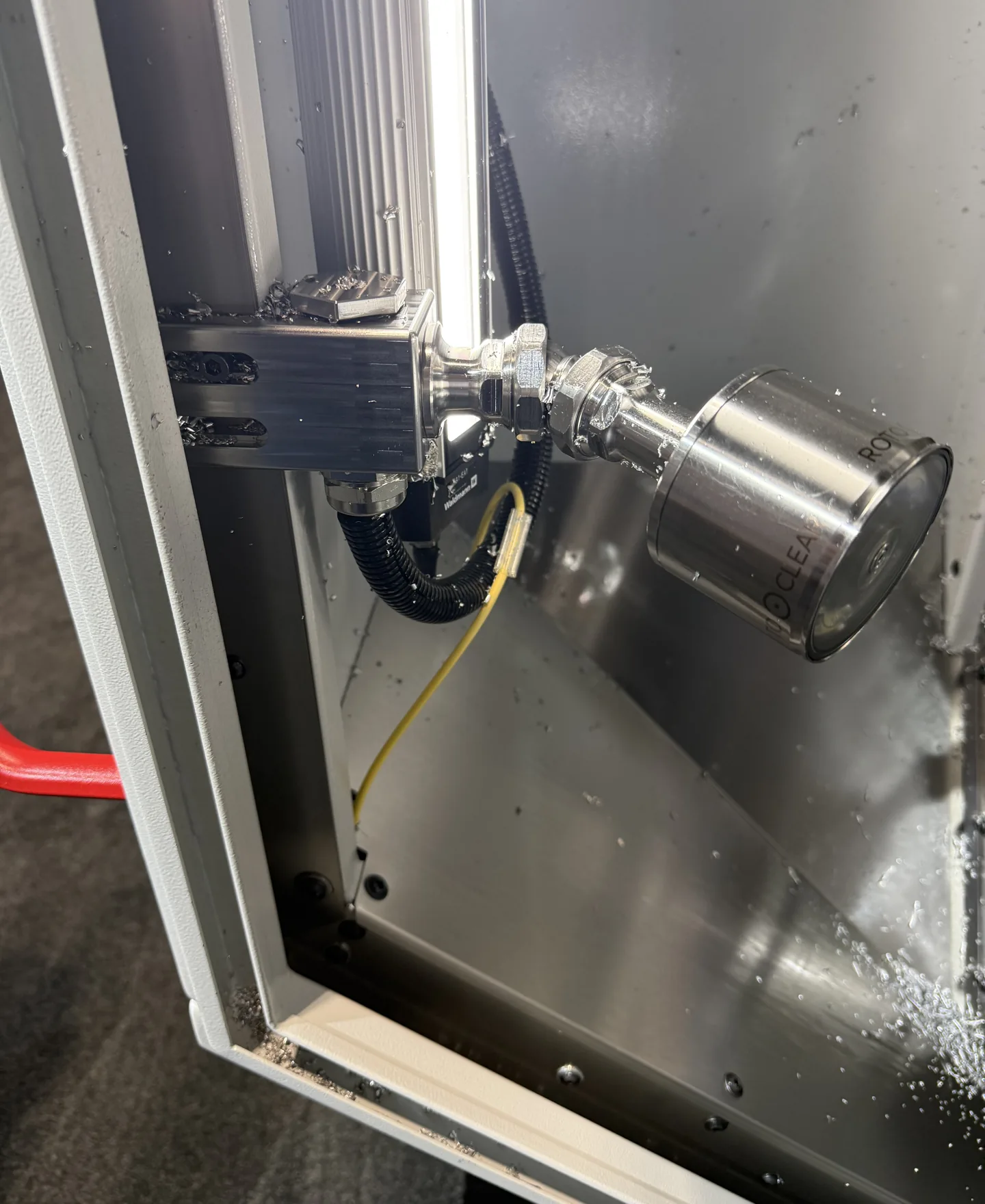 Rotoclear camera head mounted inside a machine enclosure, coolant and chips on the surrounding sheet metal